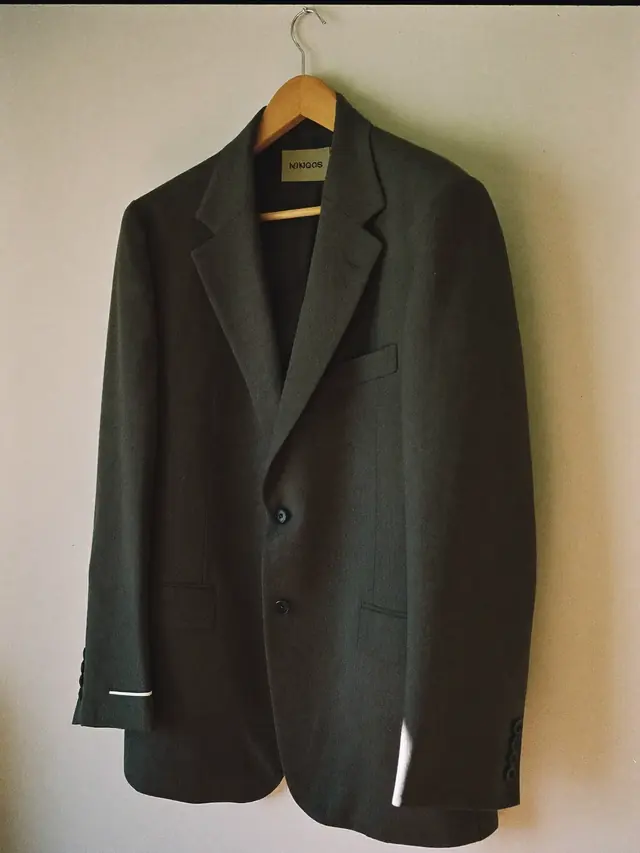A suit jacket on a hanger, pinned at the sleeve for alteration