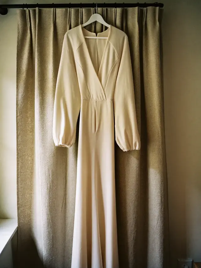 A long ivory occasion dress hanging in front of a fitting curtain