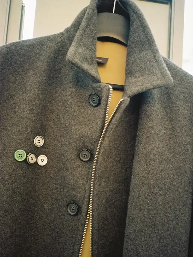 A wool overcoat with a replacement zip and buttons laid beside it