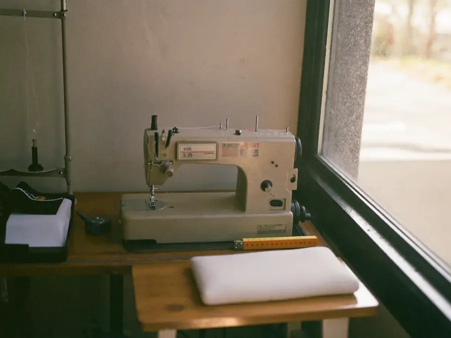 A sewing machine on a wooden bench beside a window in an alterations workroom